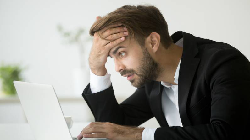 Worried stressed businessman in suit shocked by bad news using laptop at work