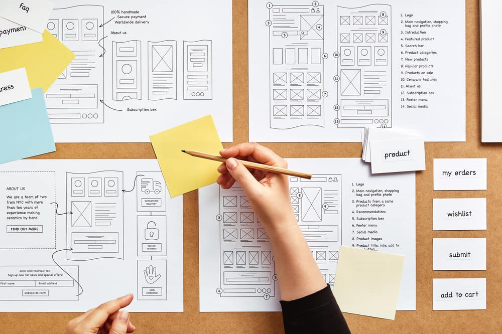 Digital and paper wireframe designs for web or mobile app UI UX display on laptop computer screen. Panoramic shot of developer workspace for brainstorming and design application framework. Scrutinize