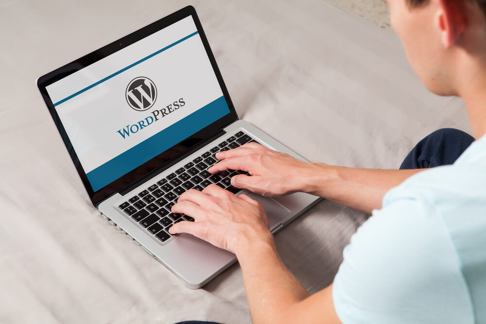 Wordpress brand logo on computer screen. Man typing on the keyboard. WordPress is a free and open-source blogging tool and a content management system (CMS).