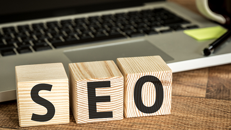 SEO (Search Engine Optimization) written on a wooden cube in front of a laptop