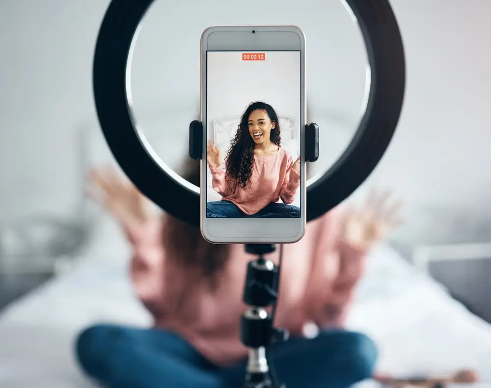 Live streaming, phone and black woman talking on video podcast in the bedroom of her house.