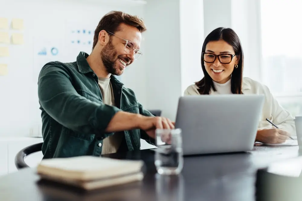 Two business people using a laptop together while sitting in a meeting. 