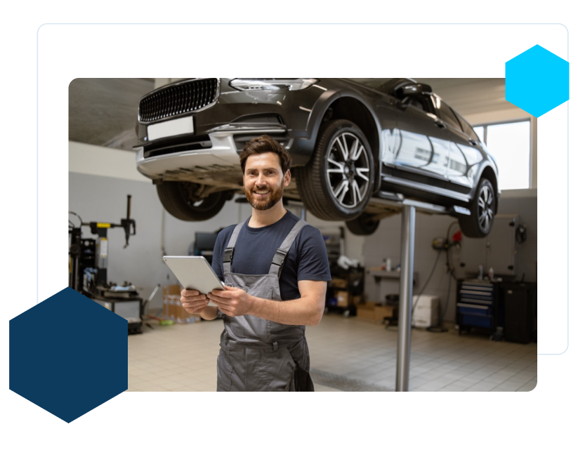 Friendly mechanic using tablet in modern car repair shop with car on lift.