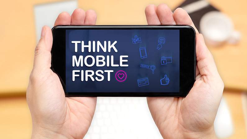 Watching two hand holding mobile phone with Think mobile first word and feature icon with blur desk office background,Digital marketing smb marketing trends.