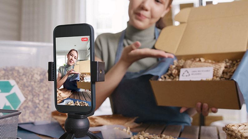 SMB owner go green net zero retail store live stream talk on phone showing eco care plastic free packaging box Asia people young woman record video on reel shop happy side hustle