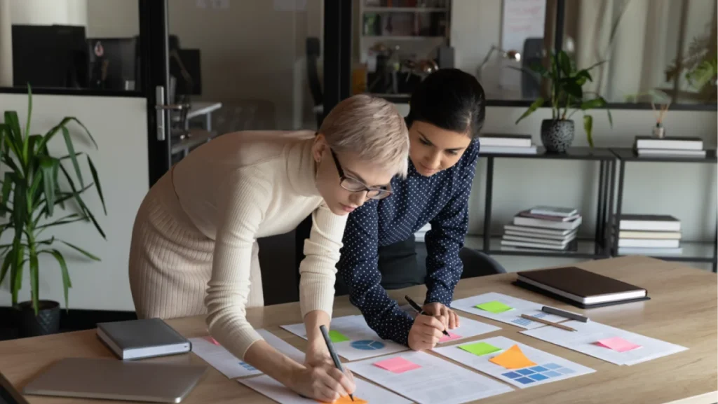 Two woman doing paper works using colorful stickers on paper documents at office table