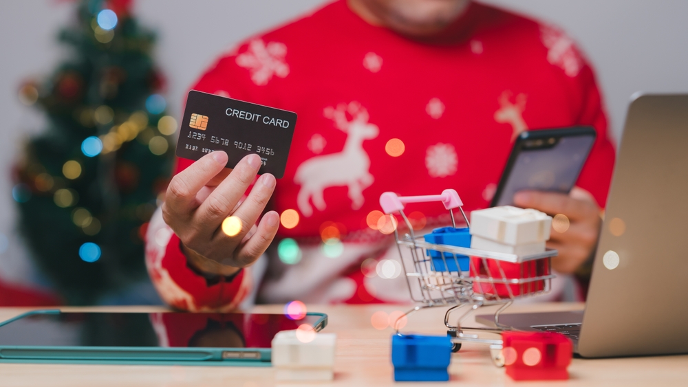 A person in a Christmas sweater holds a credit card, preparing for online shopping