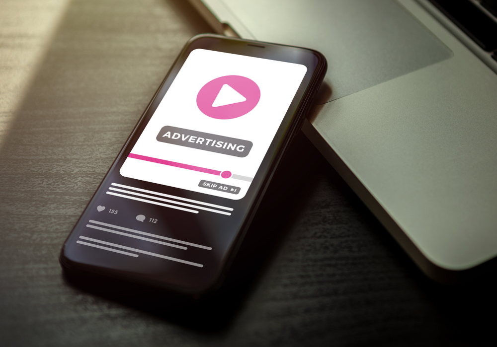 Smartphone lying on a dark wooden table with advertising media on the screen.