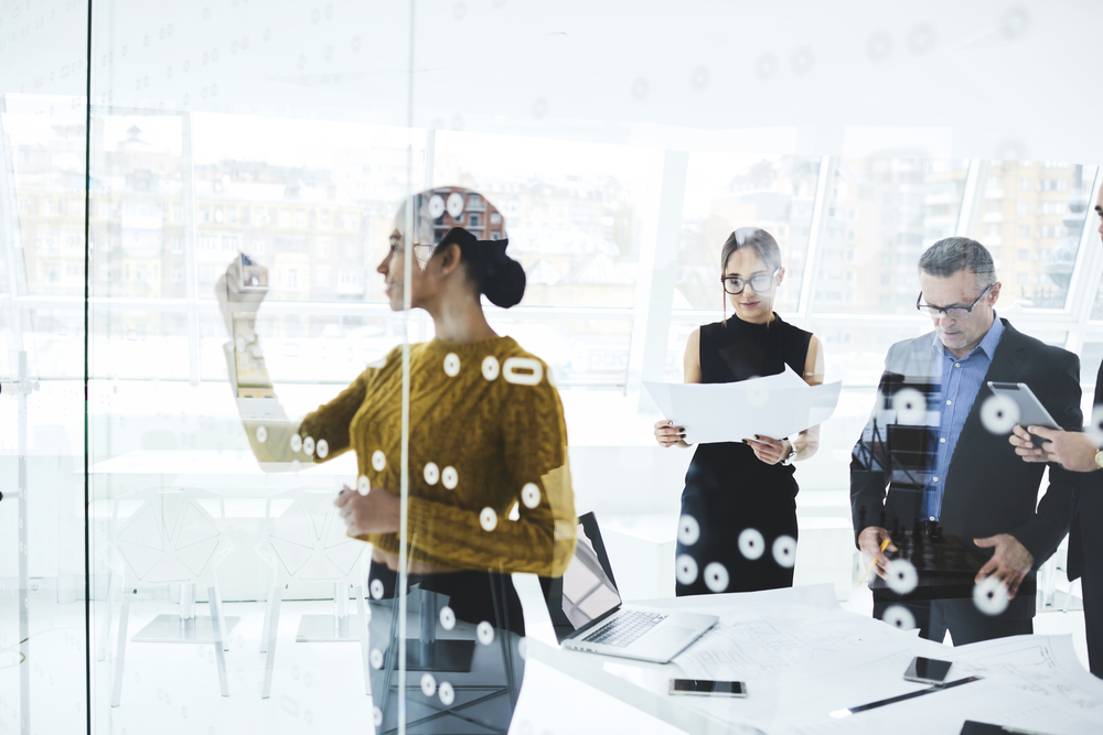 Young skilled female secretary writing on board plan with two others at the back