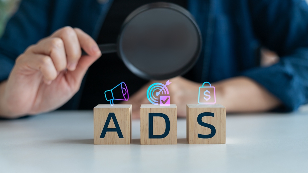 Hand holding a magnifying glass over wooden blocks with ADS text