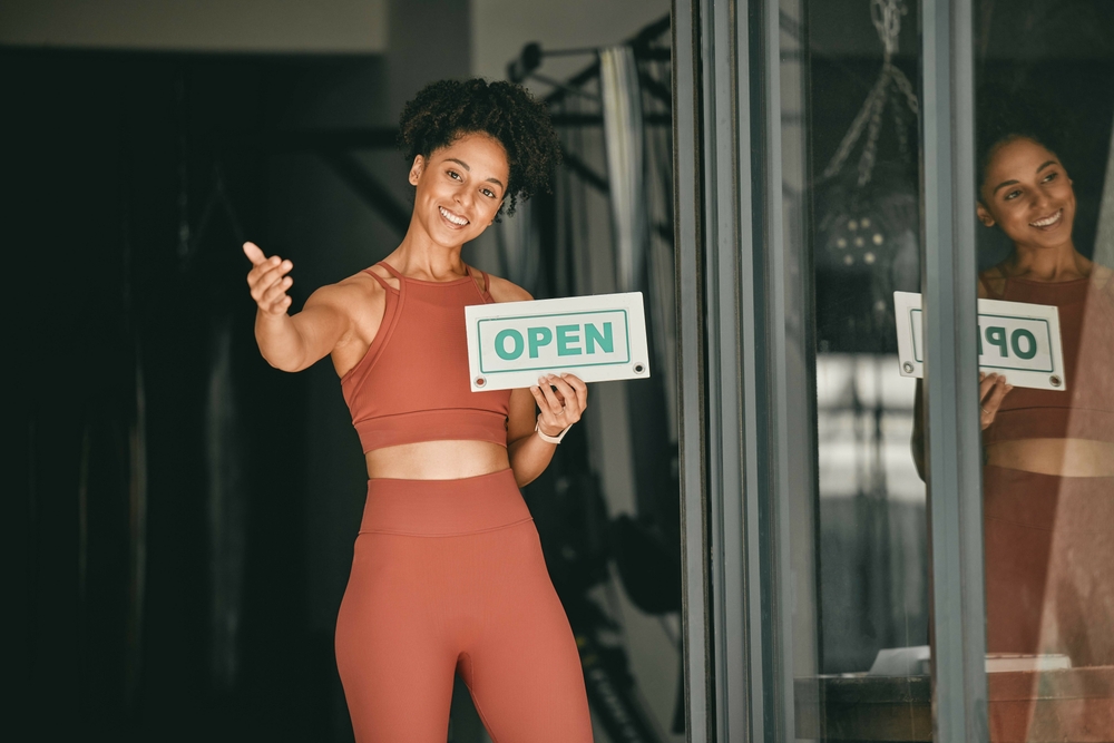 Black woman, welcome and gym owner with open sign for fitness or coaching exercise