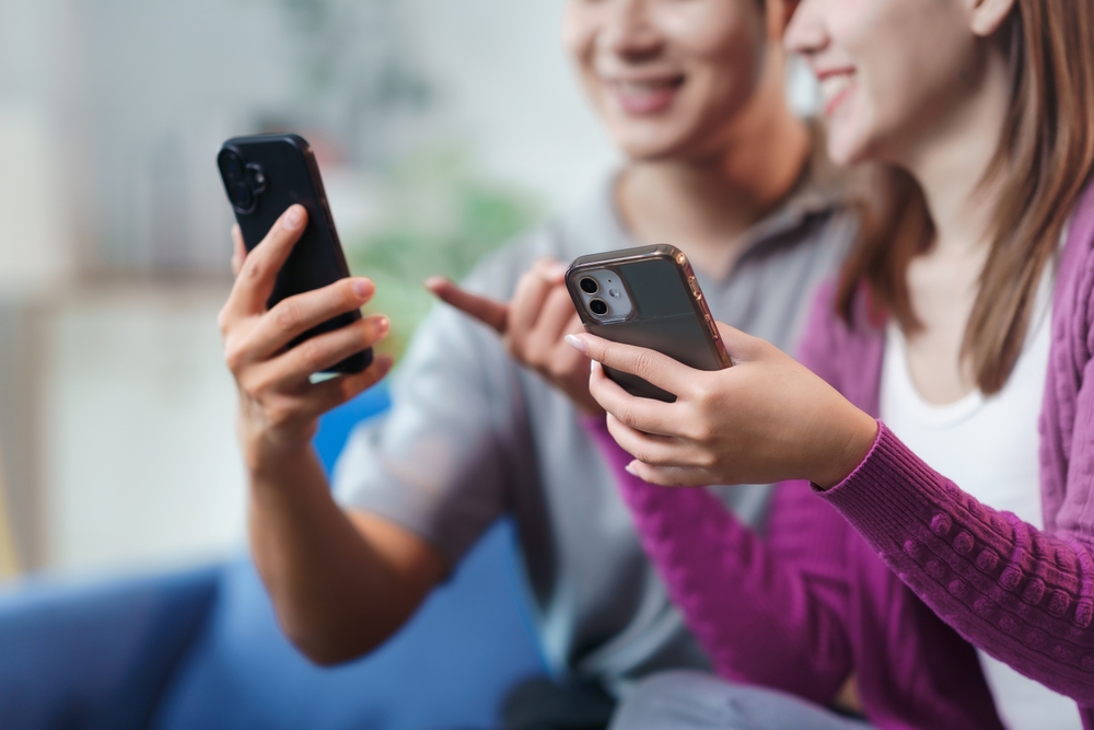 Happy couple sitting on a couch at home, using their smartphones