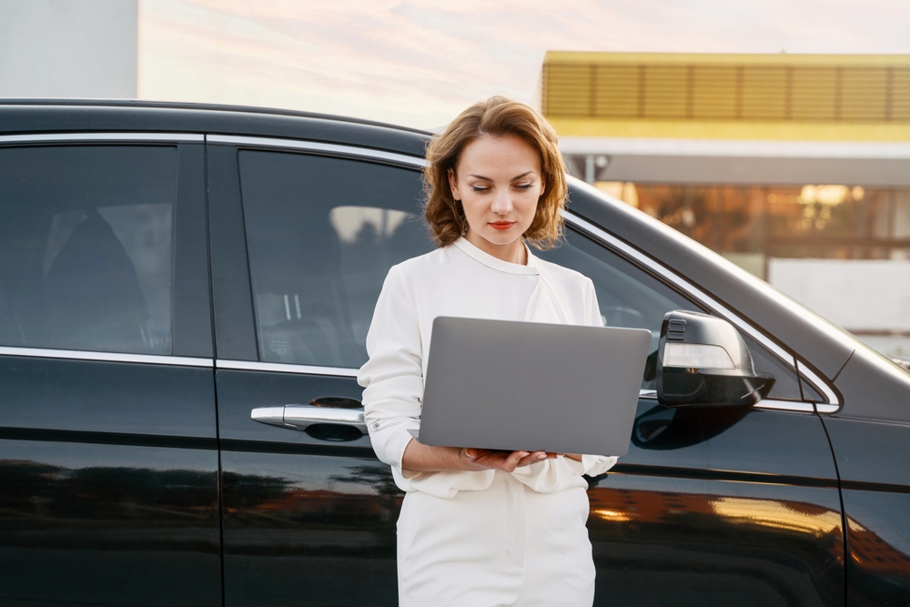 Pensive stylish businessman using laptop while working online or checking email near the car