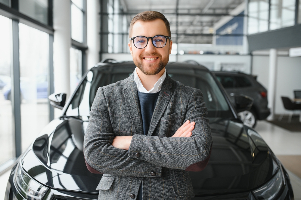 Visiting car dealership. Handsome bearded man is stroking his new car and smiling.