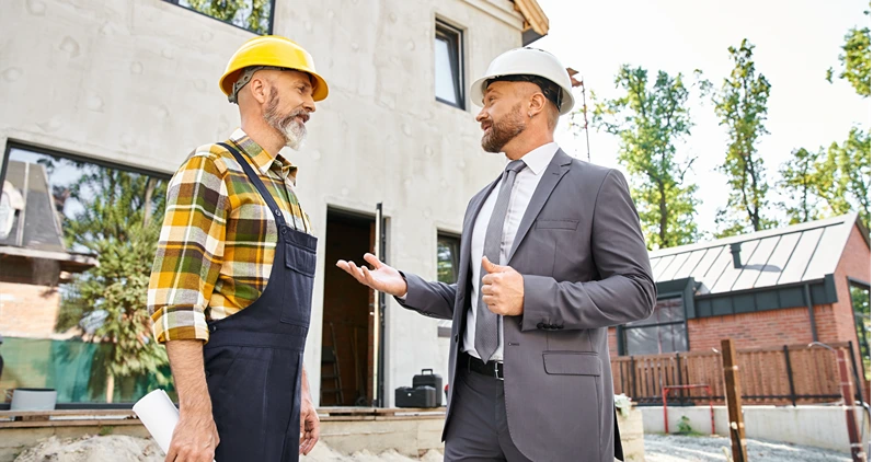 jolly cottage builder and architect in suit and overalls with blueprint discussing construction