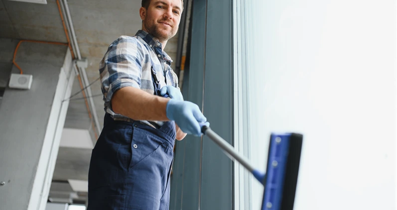 Window cleaner using a squeegee, diligently washing windows in a sleek, modern office building with a stunning glass facade