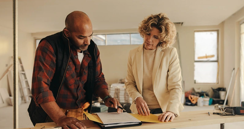 Mature contractor and homeowner signing a contract indoors for a home renovation project. They demonstrate professionalism and dedication to their work, ensuring a successful remodelling experience.