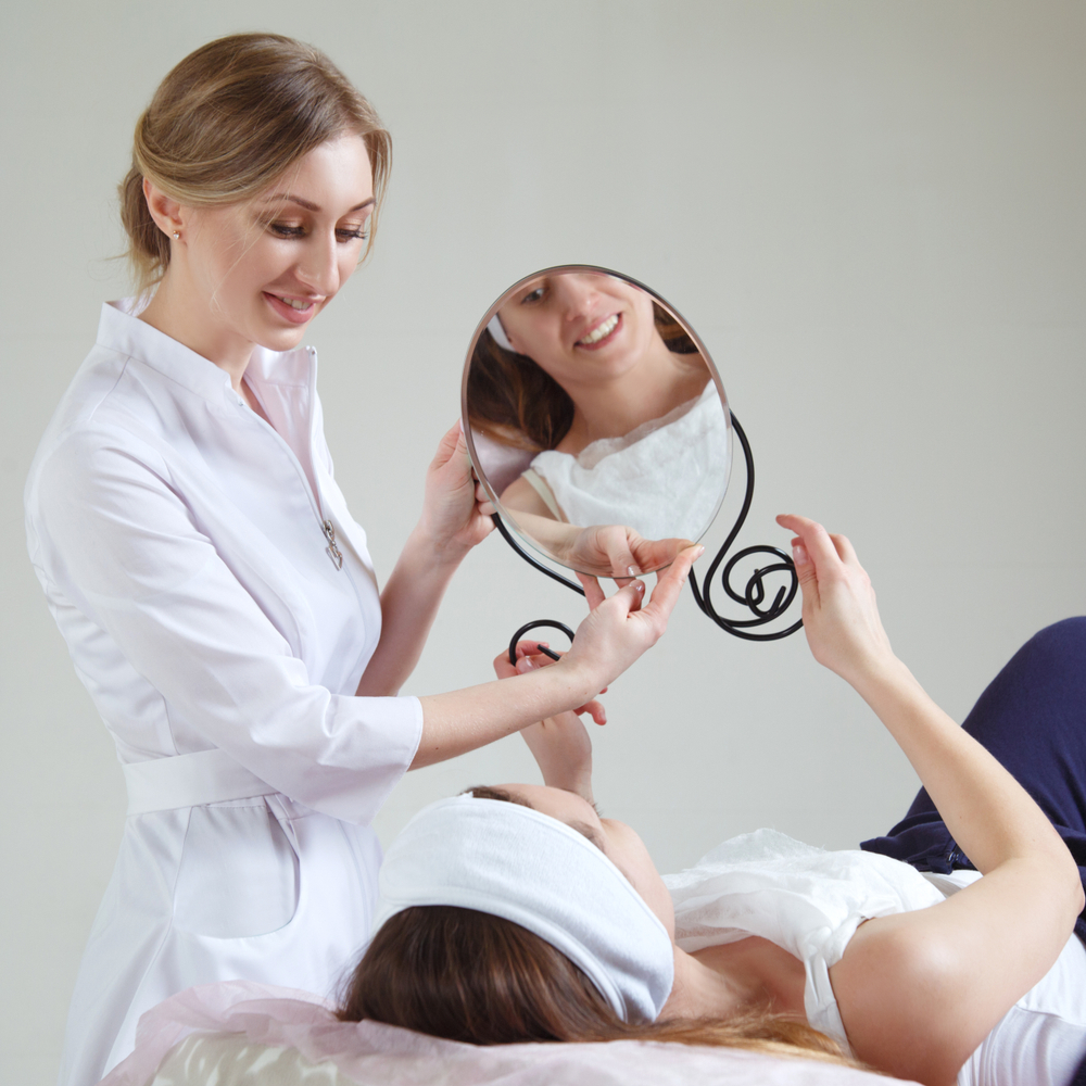 A cosmetologist and a patient discuss the upcoming procedure in front of a mirror.