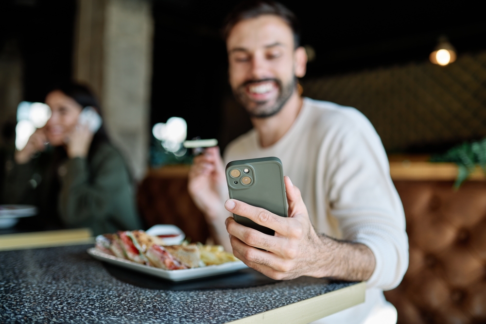 Portrait of a young romantic couple in restaurant having lunch and using a mobile phone