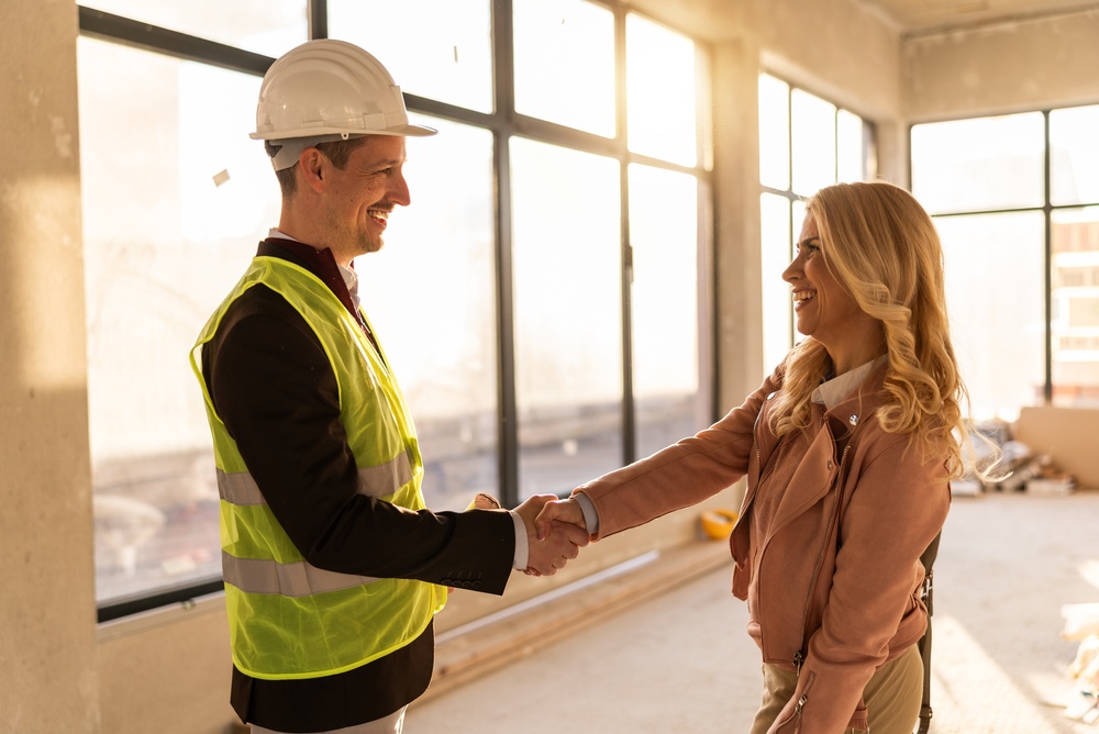 Two professionals shake hands inside a construction site of an office space.