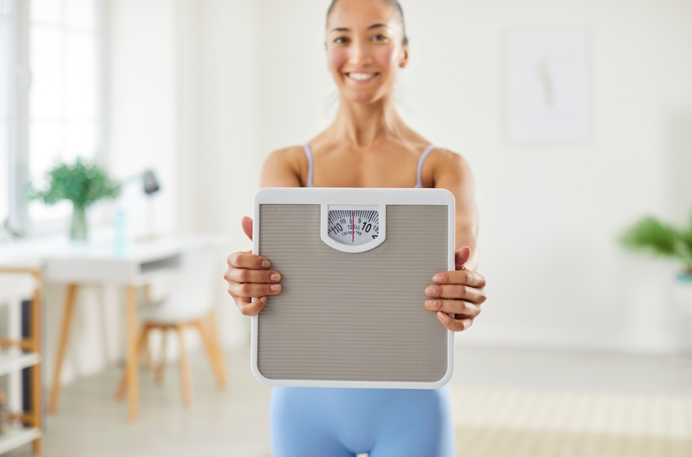 Portrait of a young happy smiling sporty slim woman holding scales in hands after measuring her weight