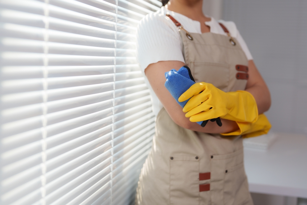 Professional cleaning lady wearing yellow gloves and holding a blue duster 