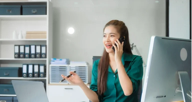 Attractive Asian businesswoman in formal business attire is working at her desk with a laptop and mobile phone, focusing on corporate law, contracts, compliance, and law firm marketing strategies.