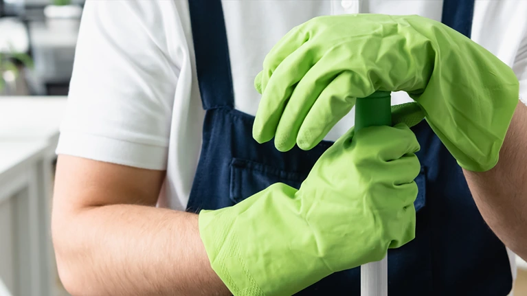 Cropped view of worker of cleaning service in rubber gloves holding mop in office, banner