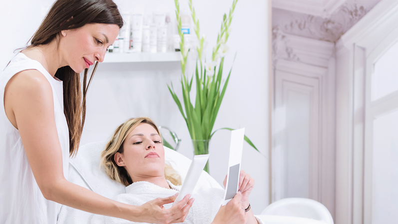 Beautiful dermatologist shows beautiful young patient cosmetics that are used at spa beauty salon.