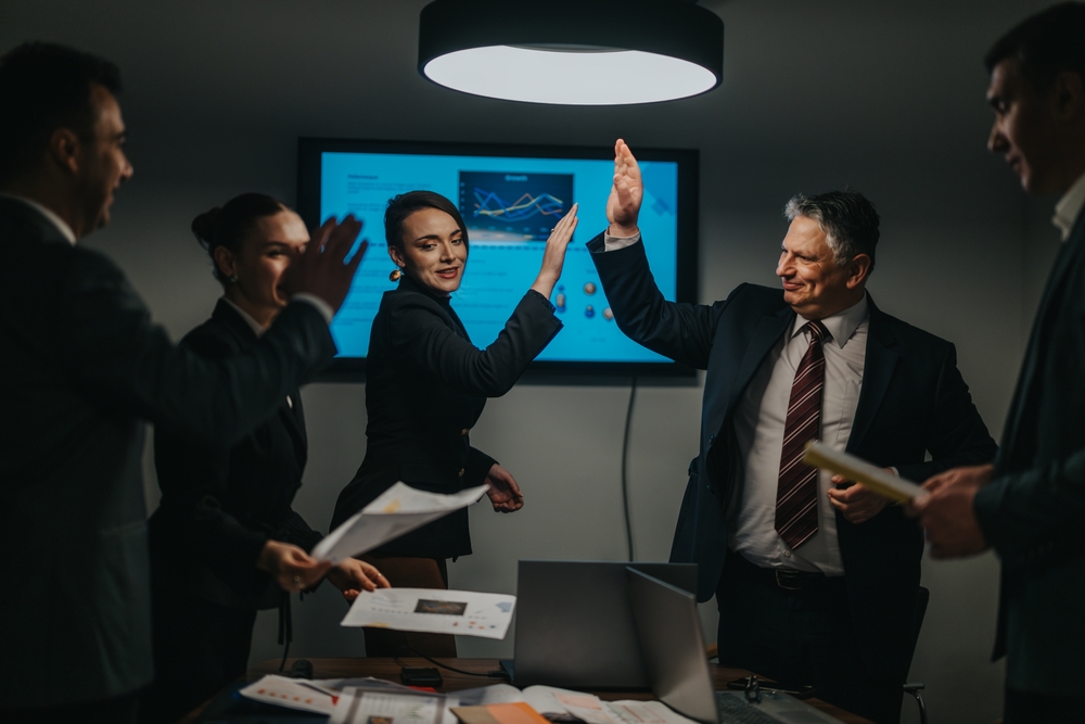 A team of professionals in formal attire high-fiving, celebrating success during a meeting. 