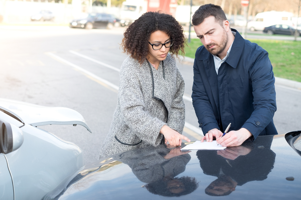Man and woman filling an insurance car form after bad car crash