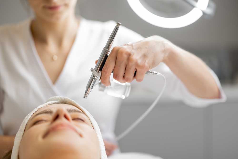 Young cosmetologist performs oxygen mesotherapy on woman's face at beauty salon.