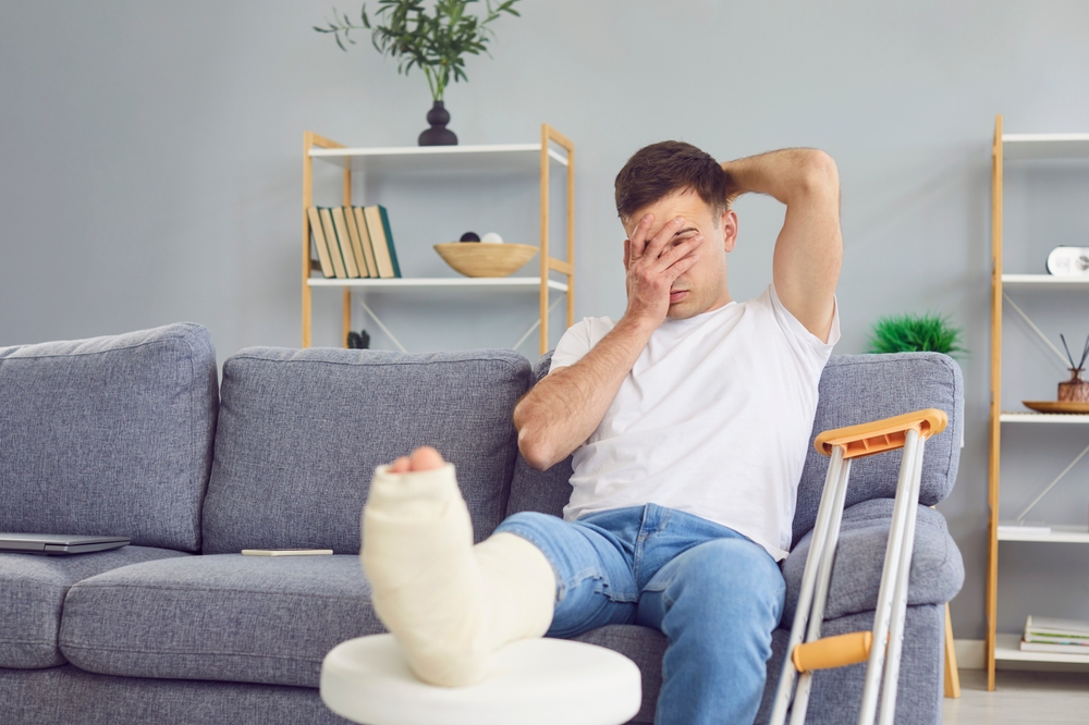 Man feeling bad pain, sad with broken leg or foot injury sitting with crutches