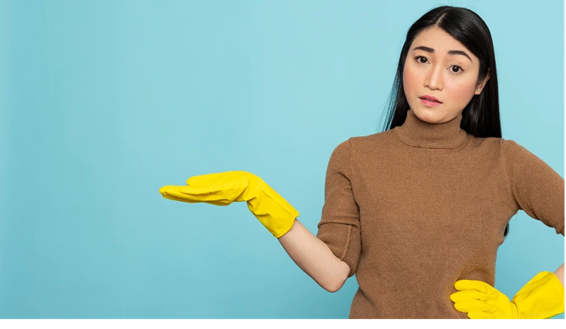 Portrait of asian woman wearing cleaning rubber gloves, hand on waist and gesturing to left side with open hand. Janitor or housekeeper posing confidently for promotional household banners.