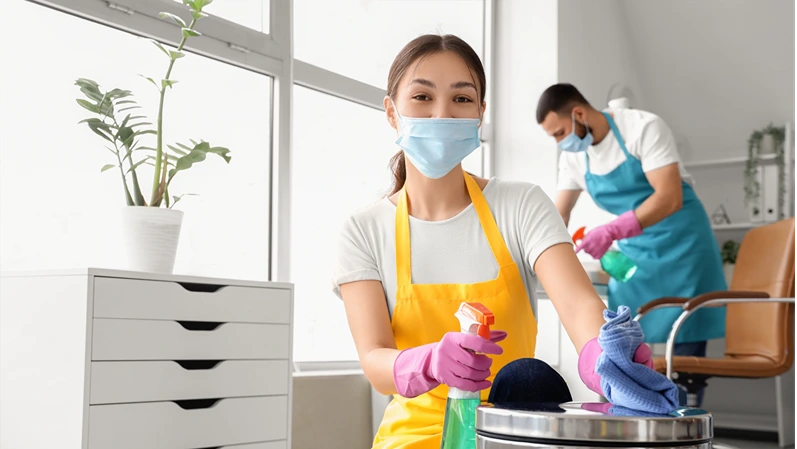 Female Asian janitor in mask cleaning bin at office
