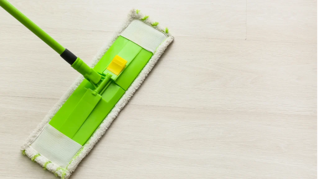 Green flat mop head with handle on light wood floor, home cleaning and maintenance