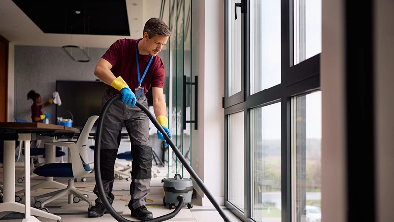 Janitorial service employee using vacuum cleaner while working in the office. Copy space.