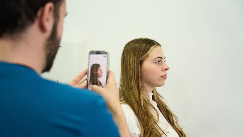 Doctor using smartphone to capture profile of young woman's face. Preparing for cosmetic treatment plan or dermal filler procedure