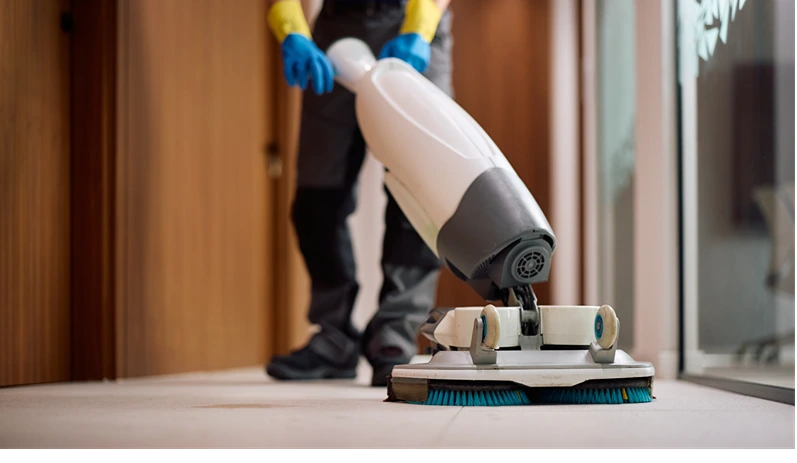 Professional janitor cleaning grey tiled floor, applying cleaning foam with squeegee during routine maintenance service