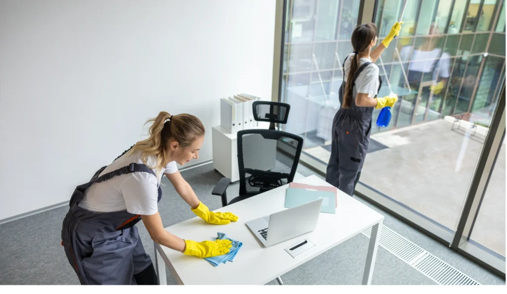 Blonde young woman in yellow gloves cleaning the table in the office