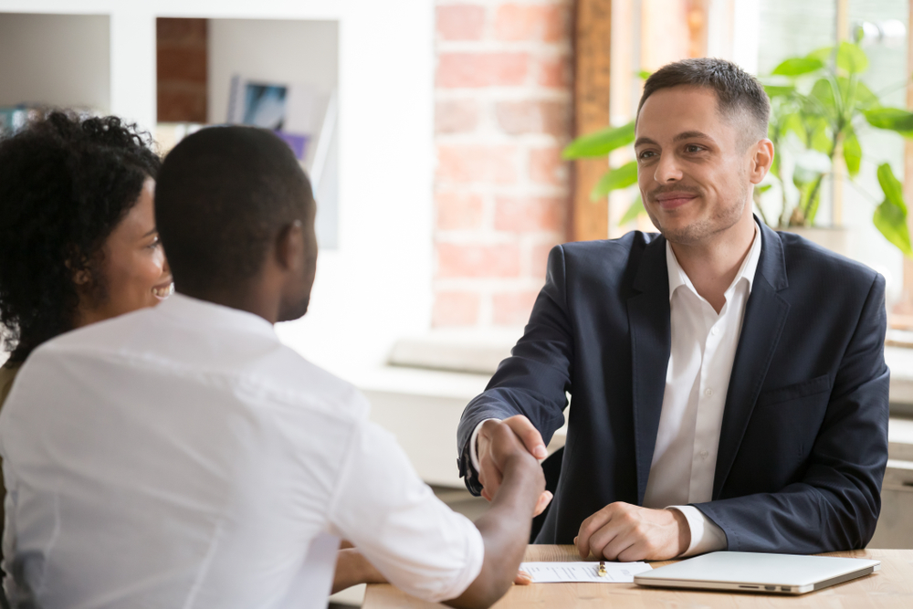 African American couple shaking hand of manager, realtor, insurer at meeting in office