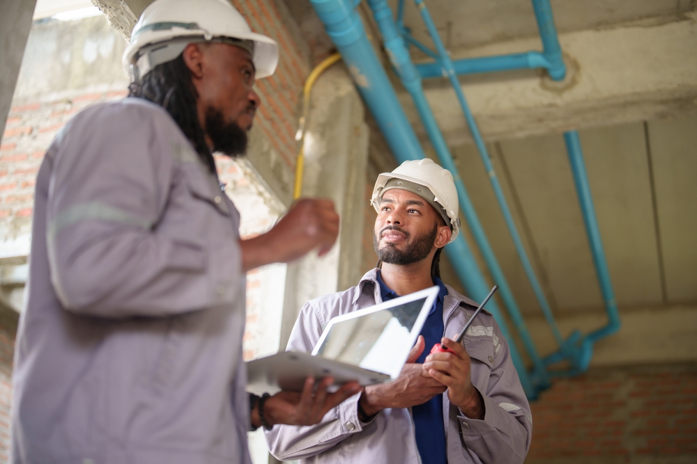 African American male construction workers or engineers or Contractors in safety helmets discussing plumbing installation